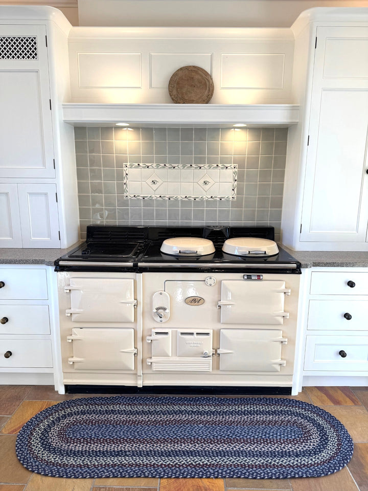 Lupin Blue Rectangle Organic Jute Braided Rug placed in a stylish kitchen with a cream stove and grey tiled backsplash.