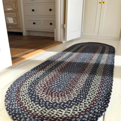Lupin Blue Organic Oval Jute Braided Rug showcasing muted colors and braided texture in a bright interior setting.