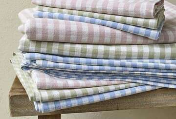 Stack of pastel gingham tablecloths in pink, green, and blue, showcasing a charming, rustic dining style.