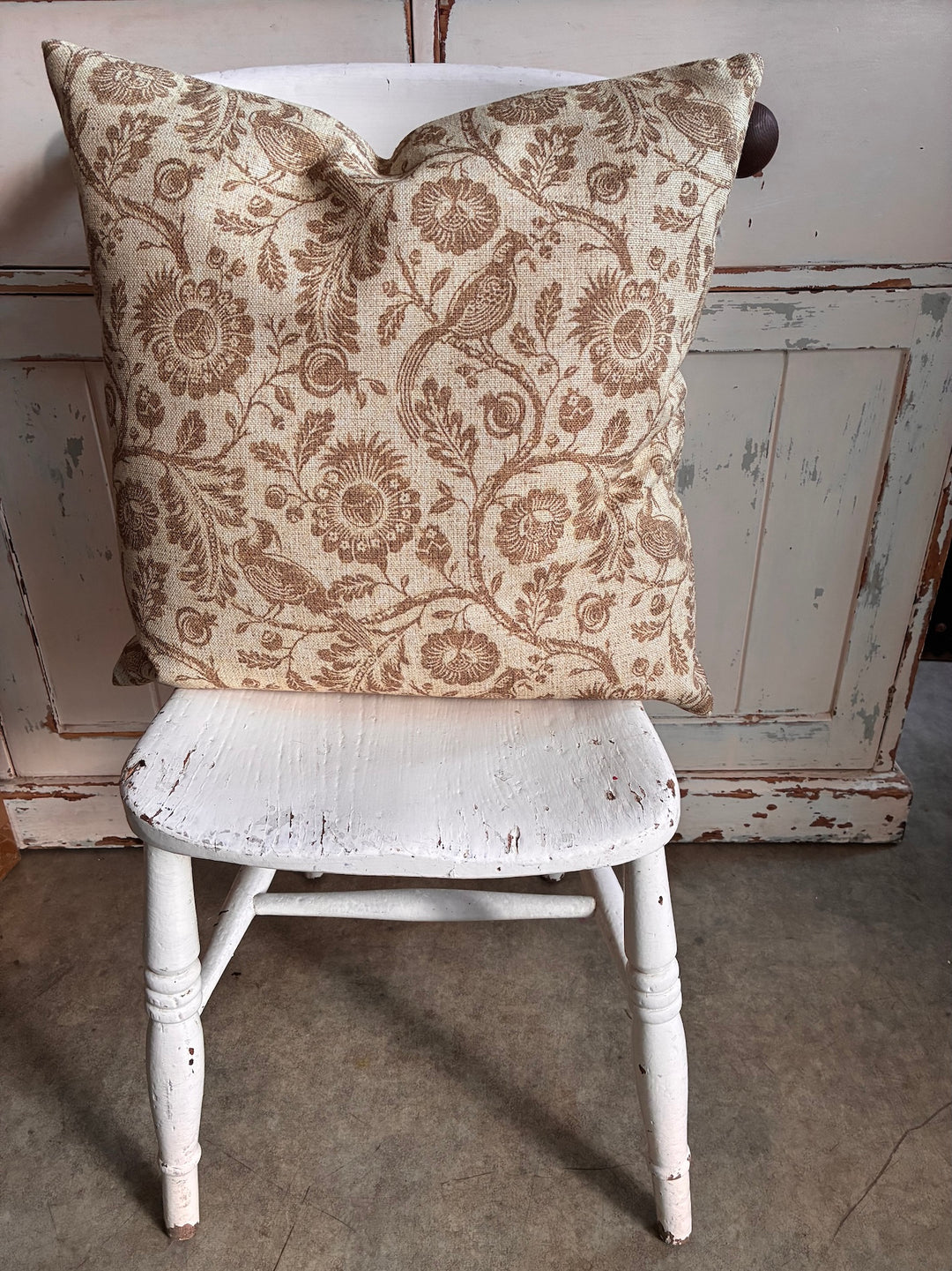Decorative pillow with floral pattern on a white wooden chair against a rustic background