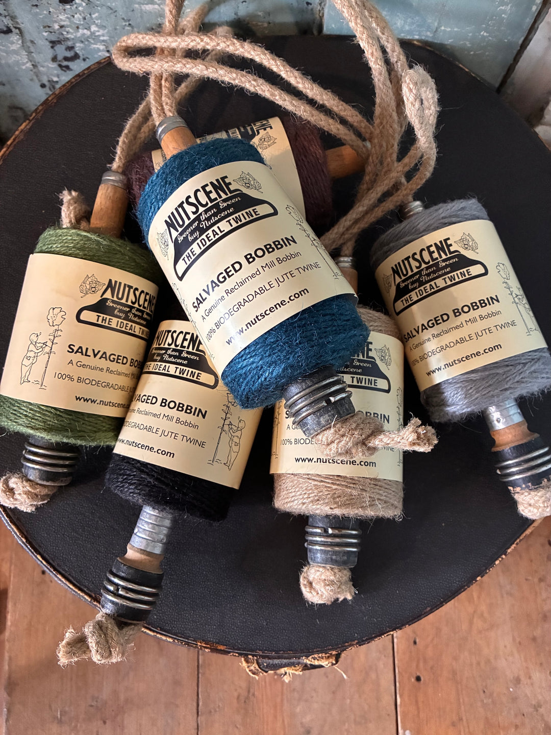 Nutscene Jute Twine on Hanging Recycled Lancashire Mill Bobbin in various colors displayed on a rustic wooden table.