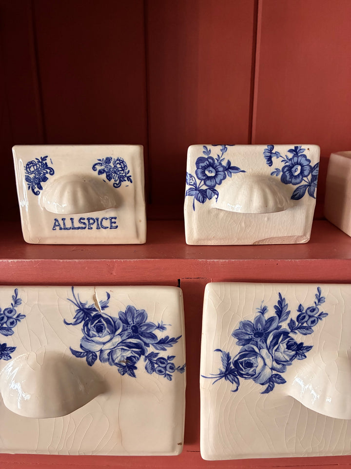 Close-up of decorative ceramic spice drawers with floral designs and 'ALLSPICE' label, enhancing rustic kitchen decor.