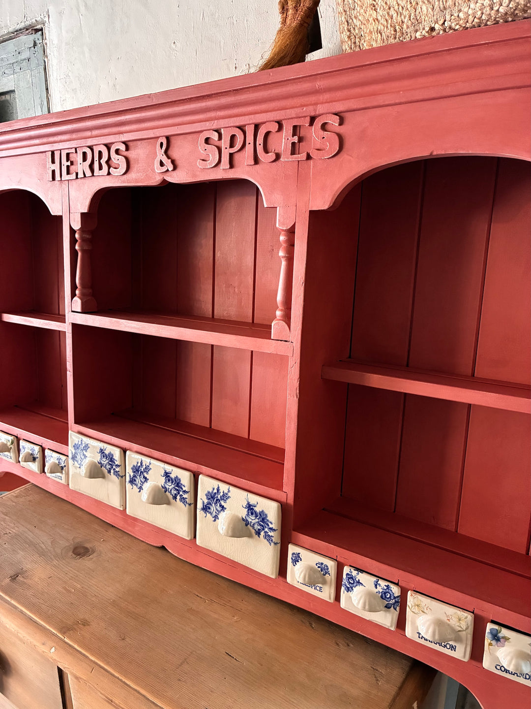 Wall mounted plate rack with herbs and spices drawers in salmon pink, featuring ceramic blue accents.