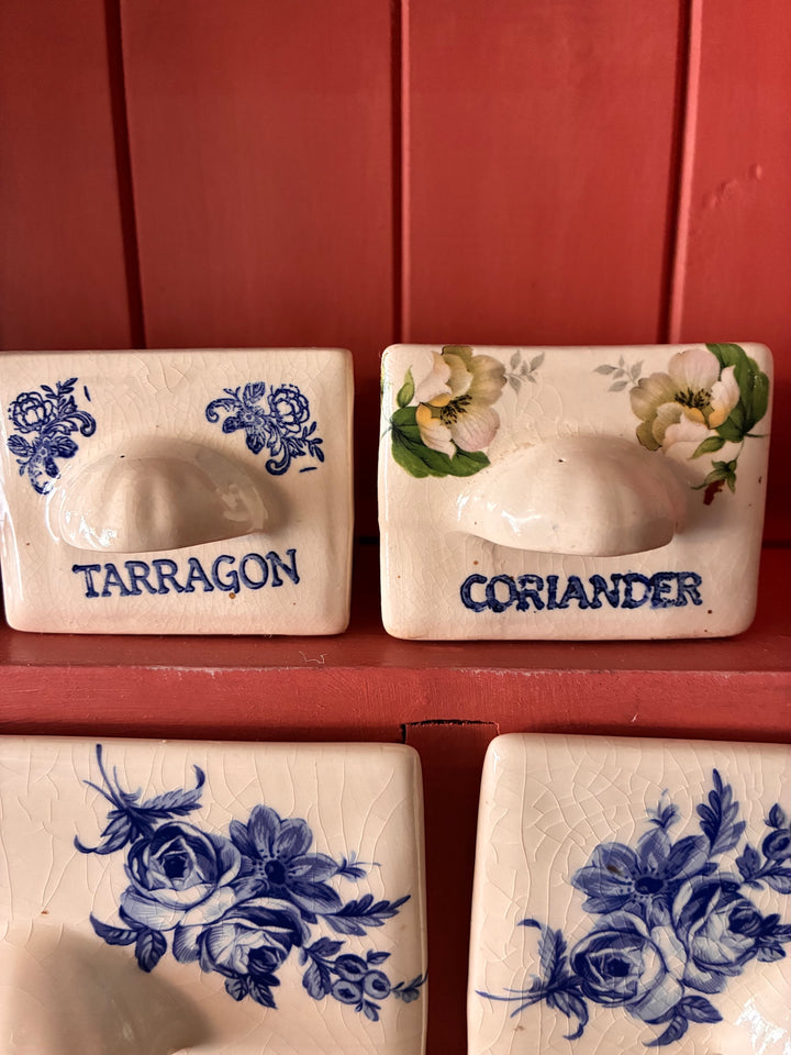 Ceramic spice drawers labeled 'Tarragon' and 'Coriander' on a rustic kitchen wall.
