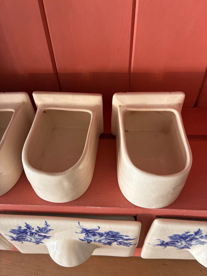 Close-up of ceramic spice drawers in beige with blue floral design, part of a rustic wall-mounted plate rack.