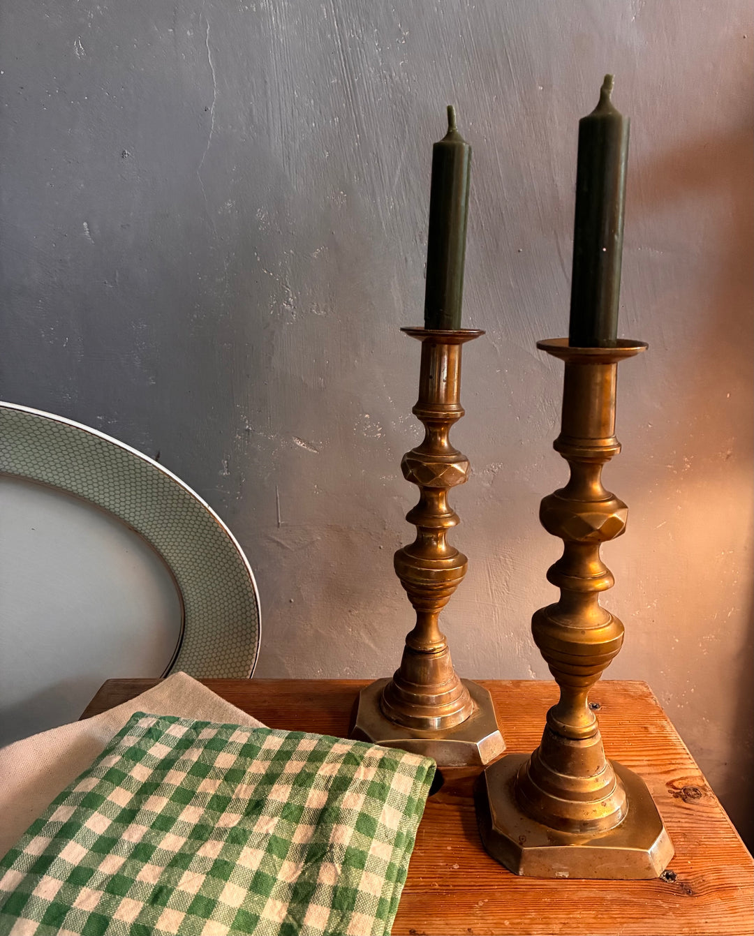 Pair of Antique Brass Candlesticks with green candles on a wooden table, showcasing their timeless elegance and character.