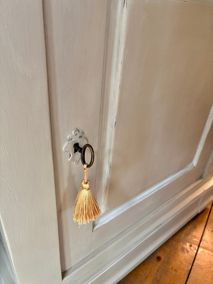 Close-up of a door handle and decorative tassel on The Manoir - Oversized Painted Side Cupboards in soft stone-grey.