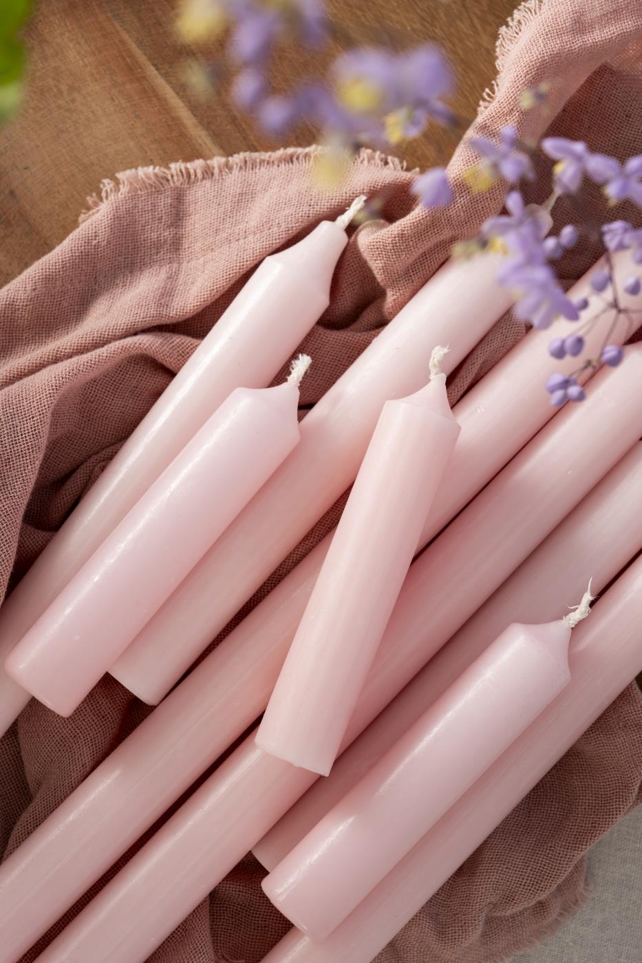 Pale Pink Stubby Dinner Candle - Bundle of Ten on a soft cloth with flowers in the background.