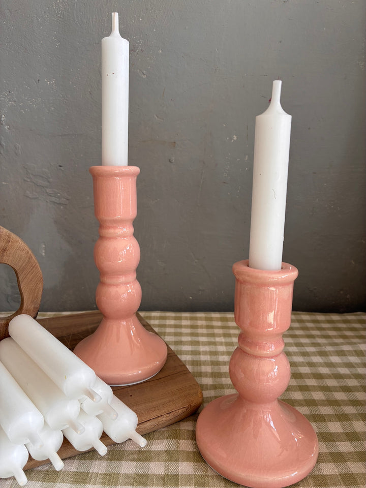 Two pink candle holders with white candles on a checkered tablecloth.