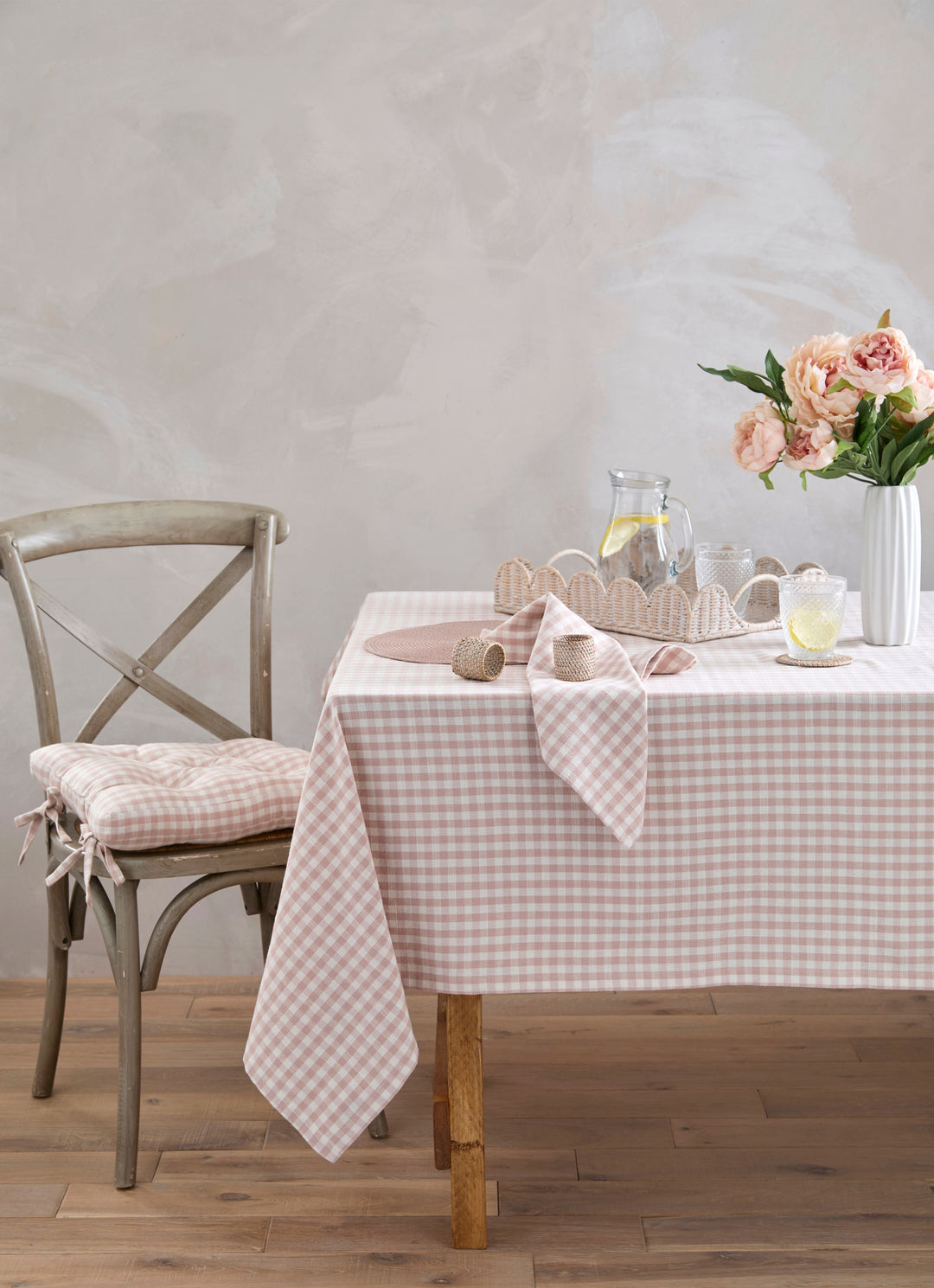 Dining table with a pink gingham tablecloth, chair, and co-ordinating gingham items against a plain wall.