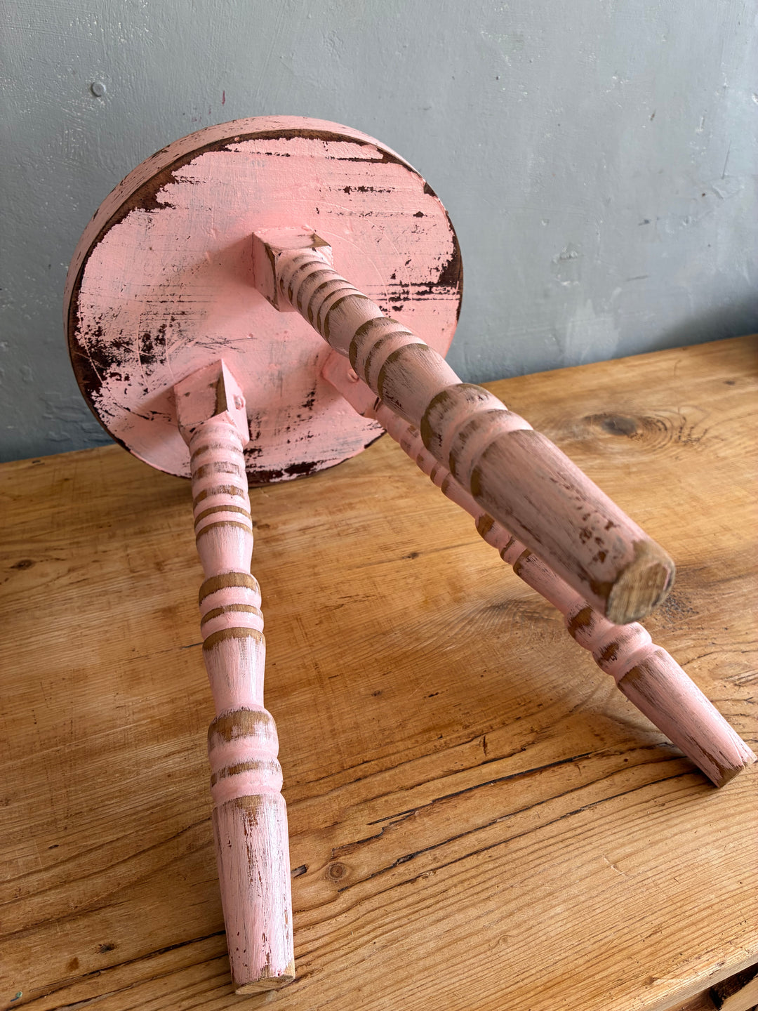 Bottom view of a Pink Vintage French Milking Stool highlighting its bobbin legs and rustic pink finish.