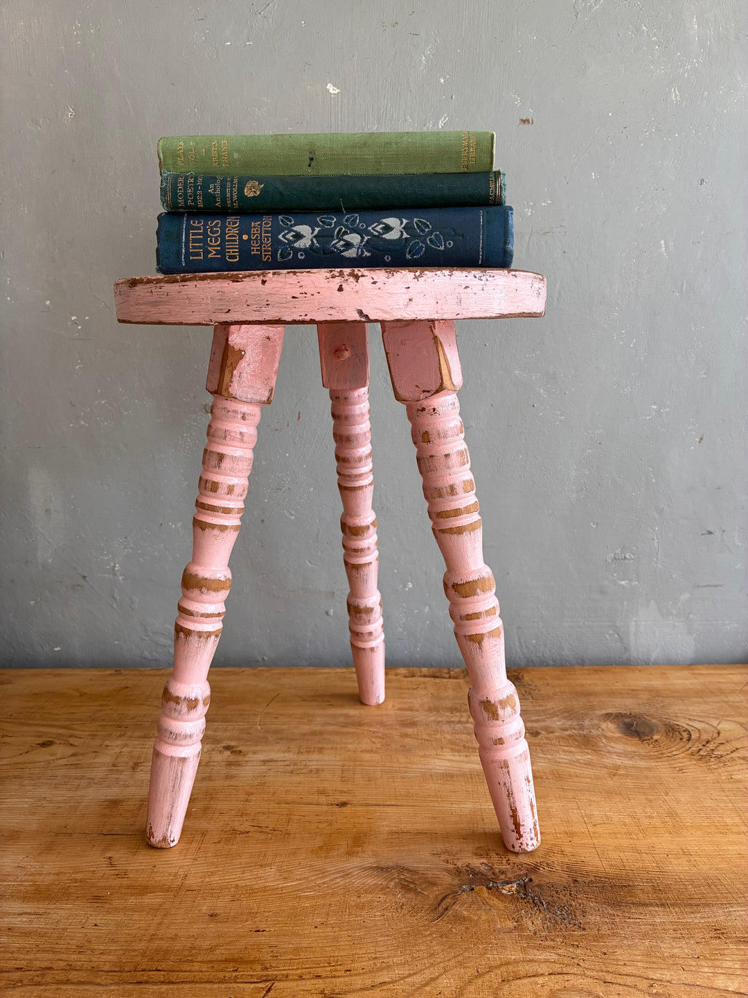 Pink Vintage French Milking Stool with books stacked on top, showcasing rustic charm and a well-worn finish.