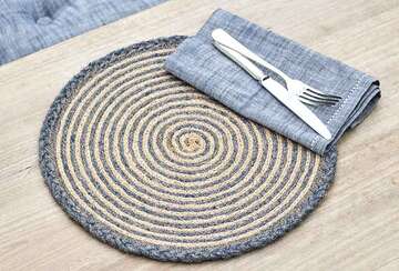 Plaited Jute Round Placemat - Indigo Blue on a wooden table with a grey napkin and silverware.