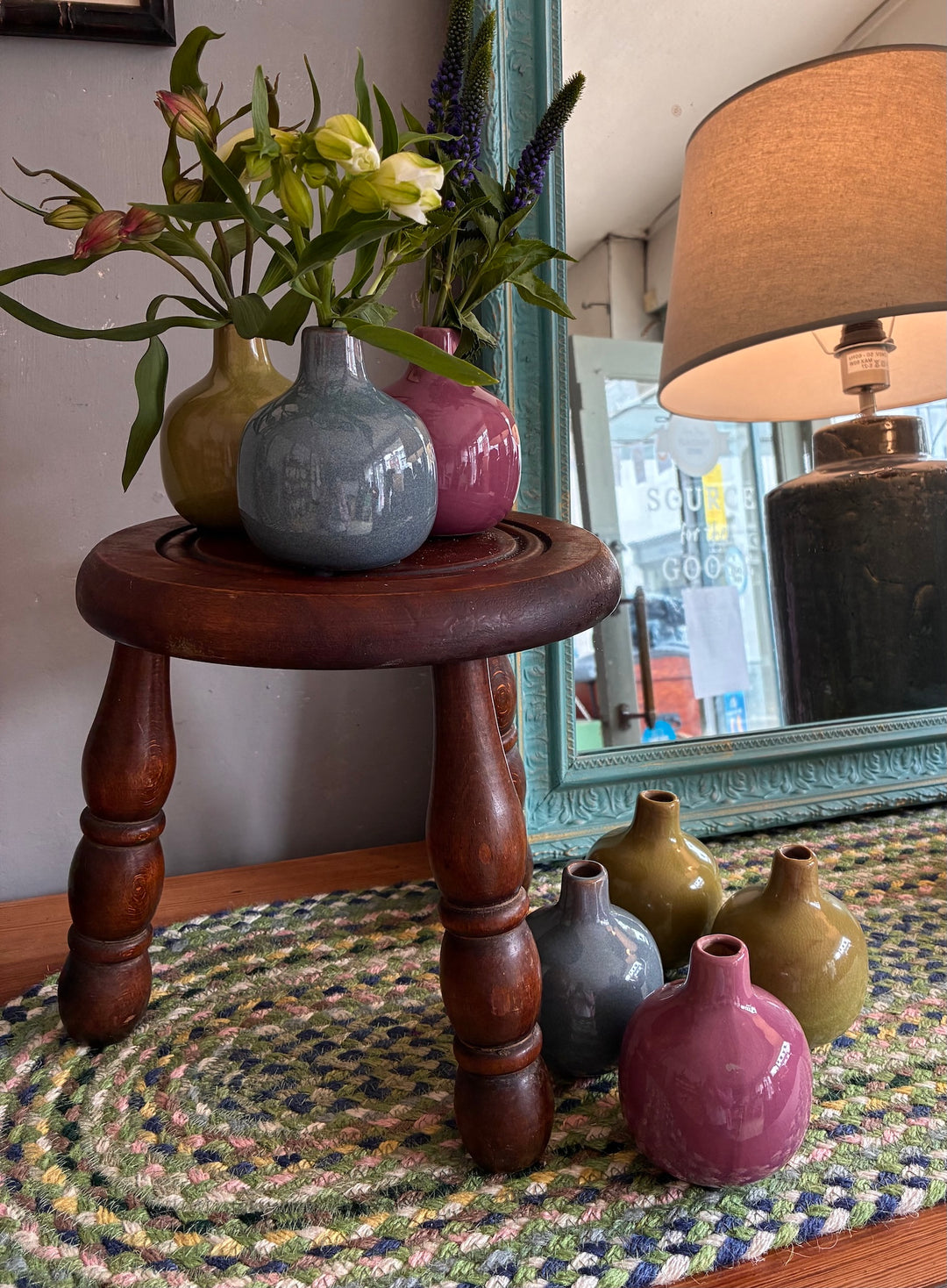 Dainty ceramic bud vases in various colors displayed on a wooden stool, showcasing home decor elegance from Source for the Goose, Devon.