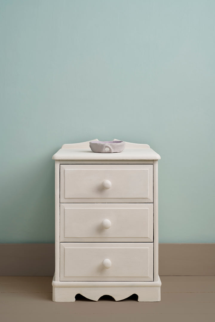 Rococo White Chalk Paint® on a white bedside table with a minimalistic design against a soft blue wall.