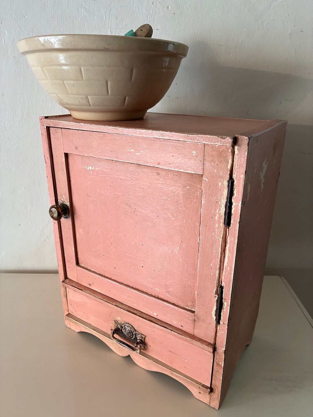 Small vintage salmon pink wall cupboard with distressed finish and old brass handle from Source for the Goose Devon.