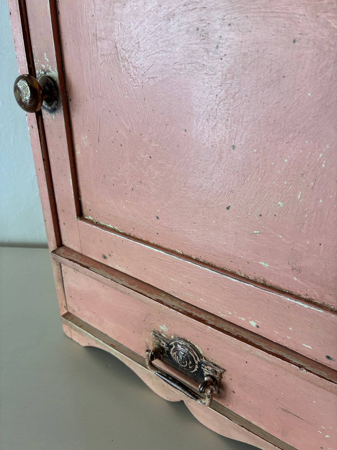 Close-up of a small vintage salmon pink wall cupboard with distressed paint and antique handles from Source for the Goose, Devon.