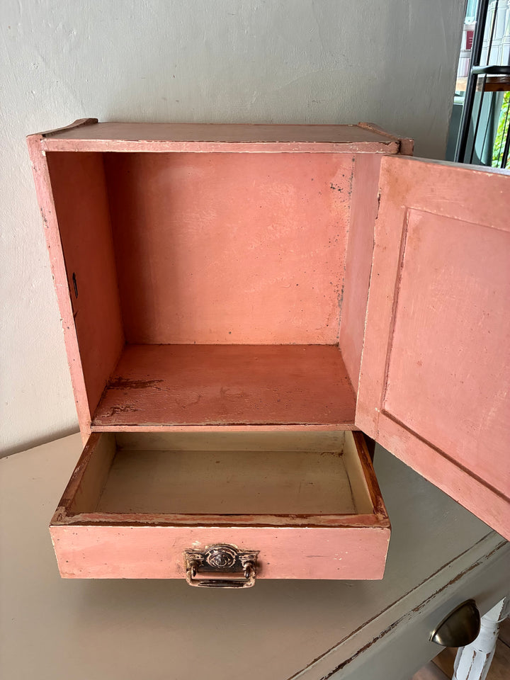 Small vintage salmon pink wall cupboard with distressed finish and brass handles, perfect for rustic kitchens and bathrooms.