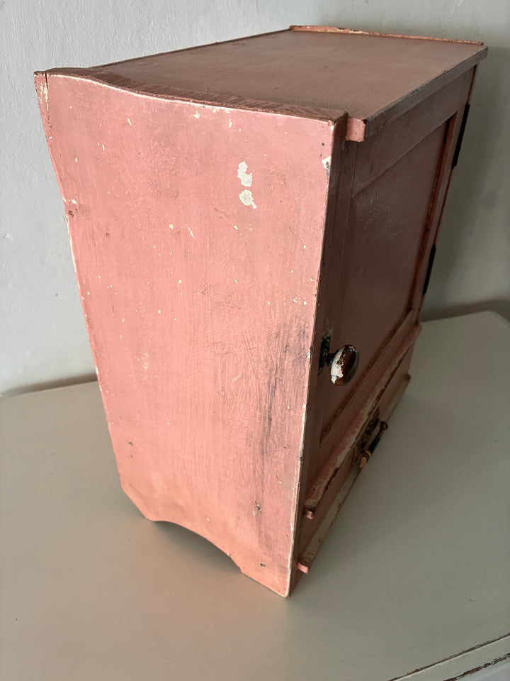Small vintage salmon pink wall cupboard from Source for the Goose, Devon, showcasing distressed paint and brass handles.