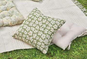 hand block printed cushion with daisy design in green and white placed on a blanket outdoors