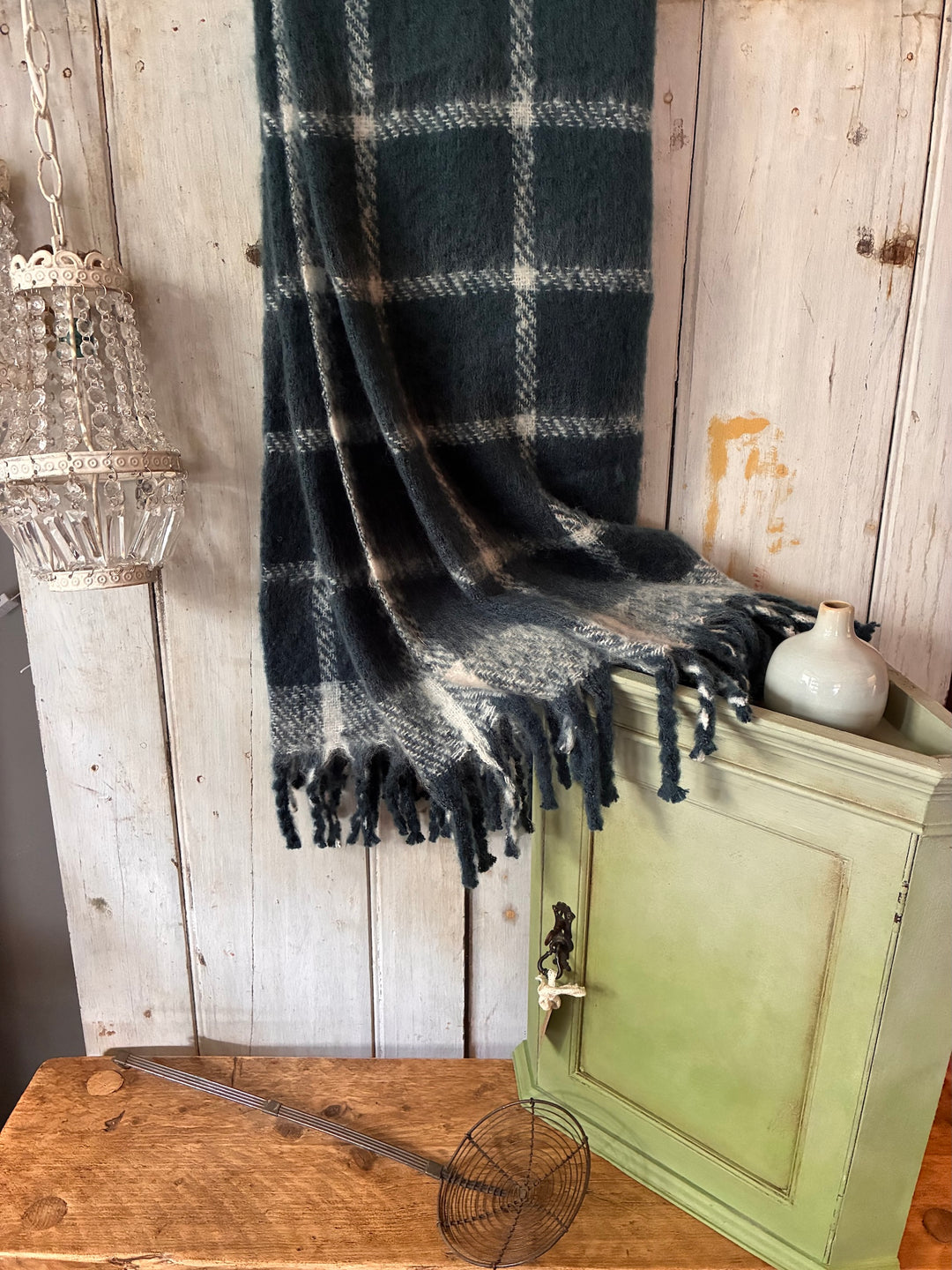 faux mohair blue throw with tassels on a wooden wall with a green cupboard in front