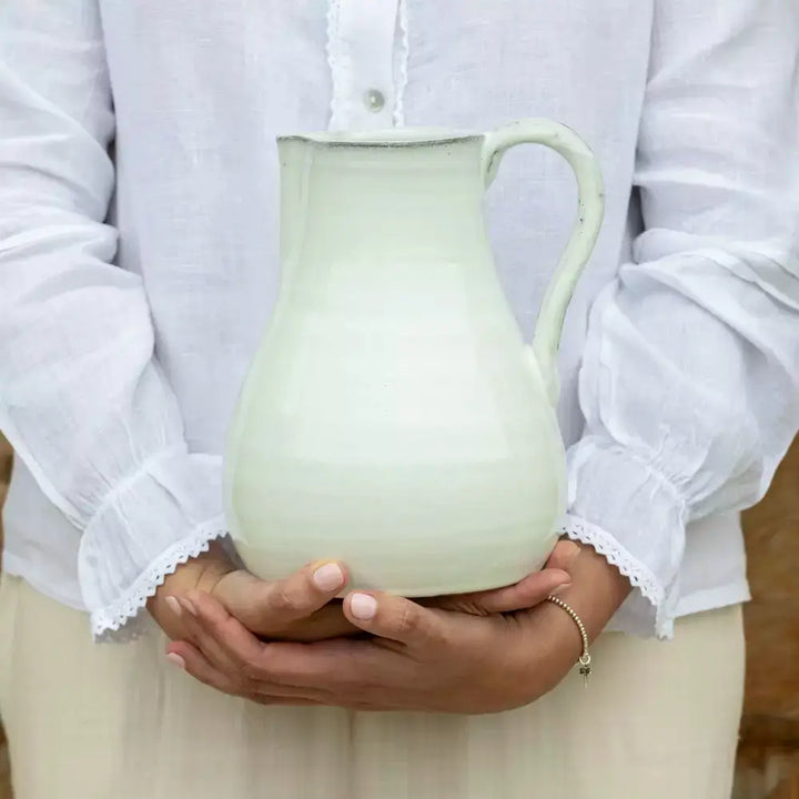 Woman holding vintage style glazed white ceramic jug with handle and spout, perfect for rustic home decor or serving cold beverages.