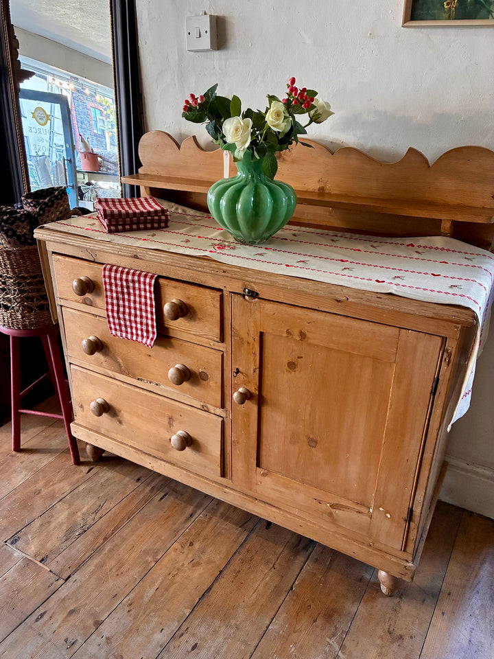 victorian antique pine dresser in the Lincolnshire dressed with a striped table runner, with a green glass vase on top with flowers and reed gingham tea towel folded on top