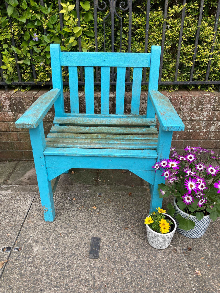 Vintage Blue Wooden Garden Chair with planters and flowers in front of garden wall 