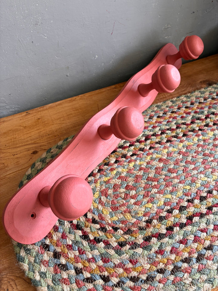 Earthy Pink Vintage French Coat Hooks displayed on a braided rug, showcasing their charming salmon pink finish.