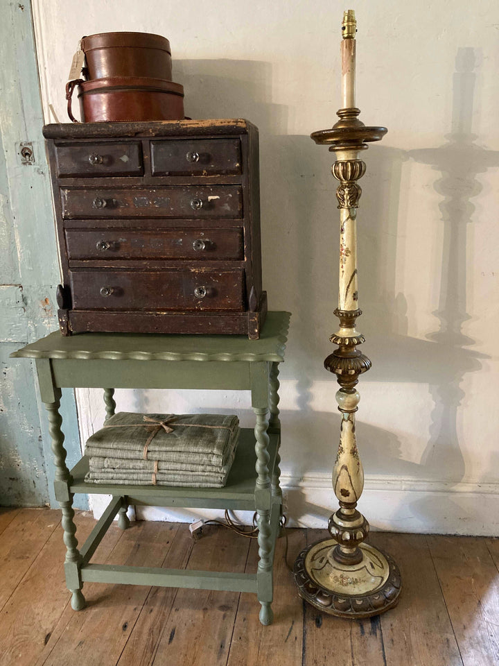 Vintage French Floor Lamp beside an apprentice piece chest on  top of a green painted table with vintage accessories
