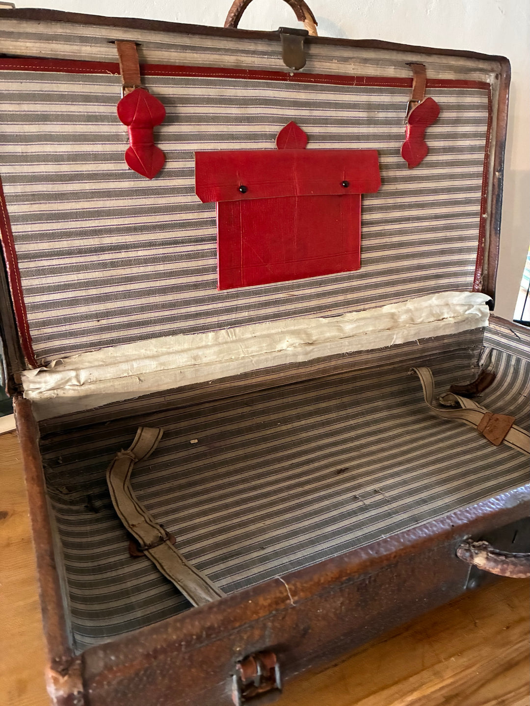 Interior view of Vintage French Leather Suitcase showcasing red leather pocket and ticking-striped lining.