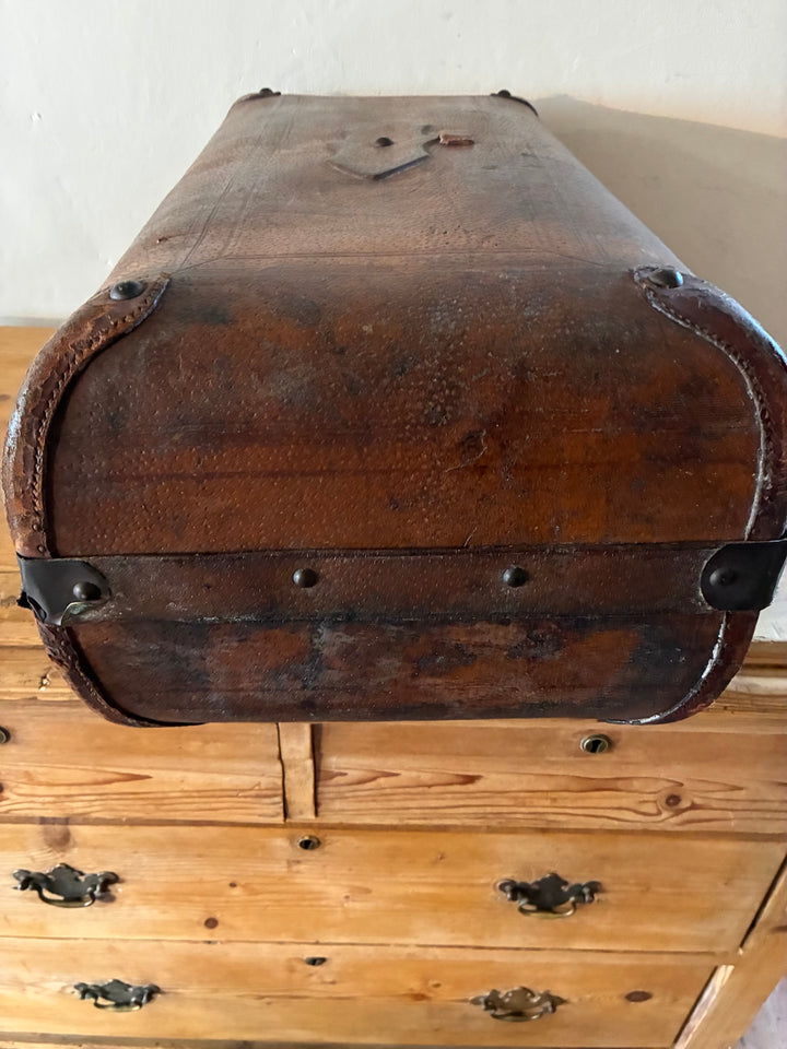 Vintage French Leather Suitcase with rounded reinforced corners and patina on a wooden surface.