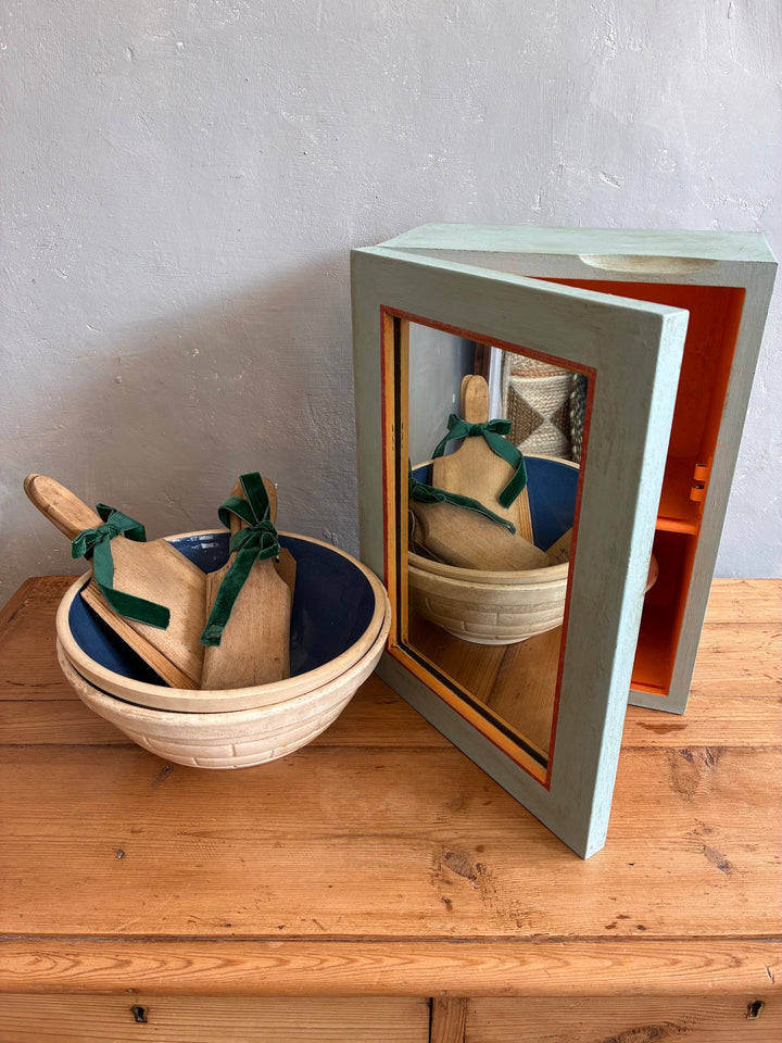 Vintage mirrored wall cabinet in soft blue with orange accents next to a wooden bowl, perfect for adding charm to any space.