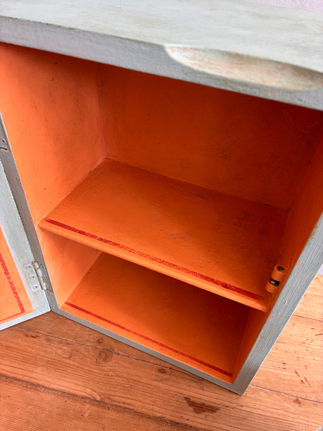 Interior of vintage mirrored wall cabinet by Source for the Goose, featuring soft blue outer and vibrant orange shelves.