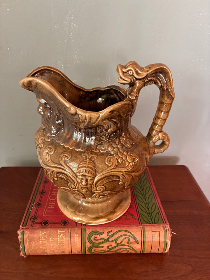 Vintage Neptune Pottery Jug displayed on antique books, showcasing intricate sea serpent handle and mythological design.