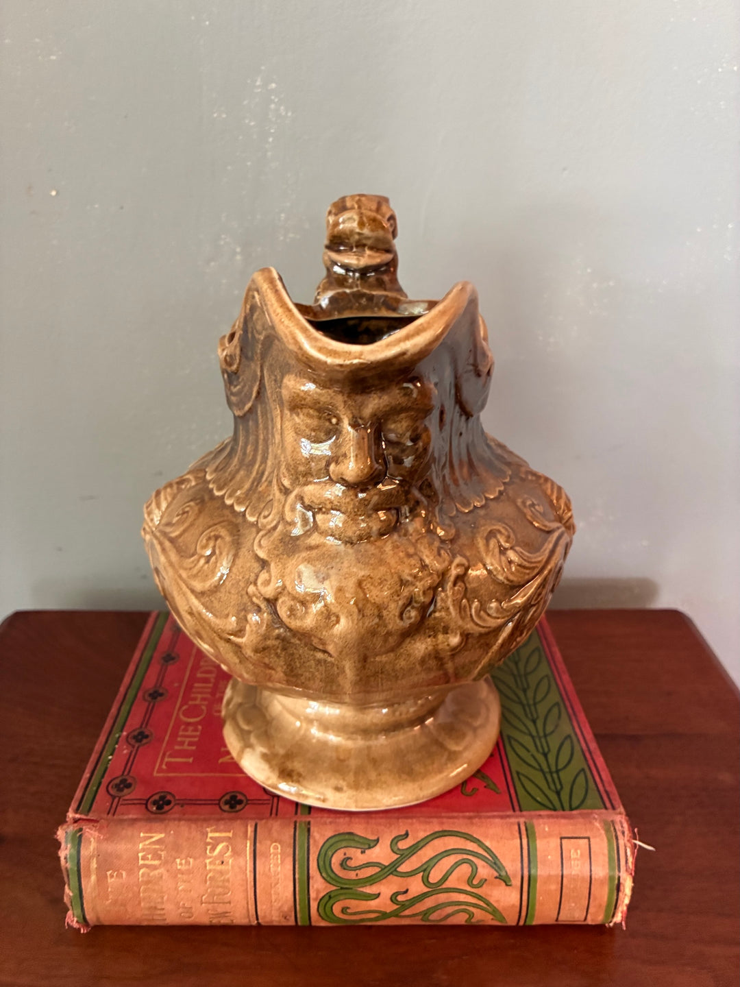 Vintage Neptune Pottery Jug displayed on a vintage book, featuring Neptune's face and sea serpent handle.