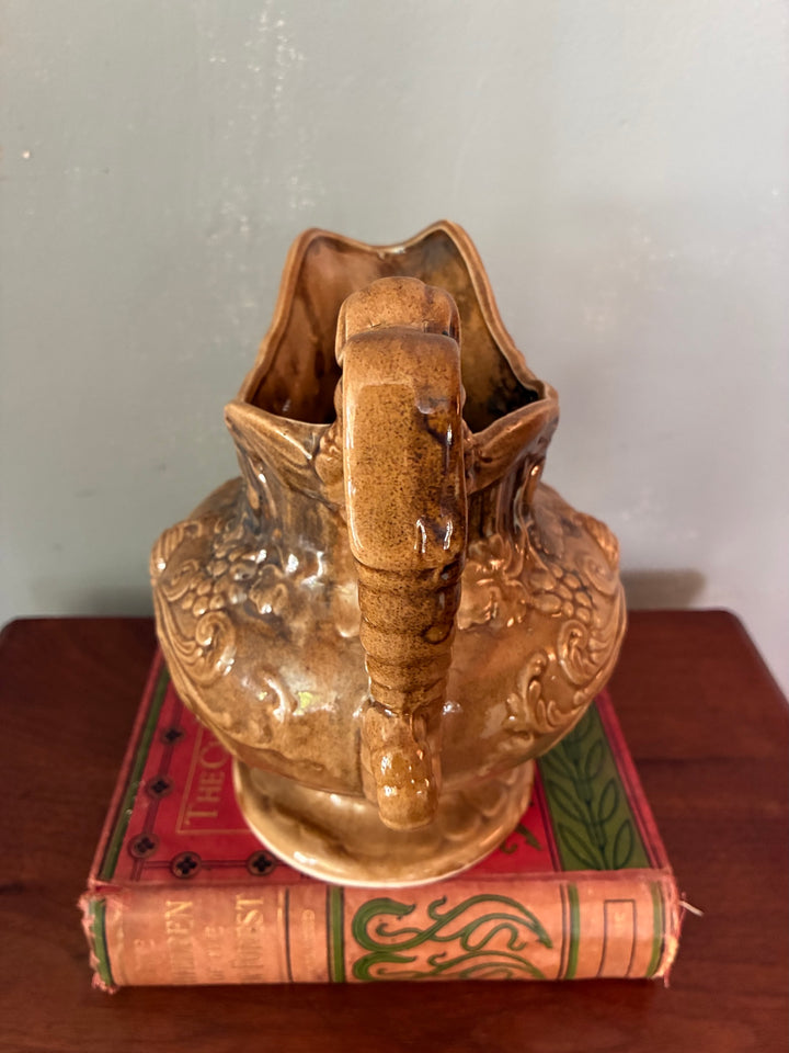Vintage Neptune Pottery Jug displayed on a vintage book, showcasing its ornate craftsmanship and nautical design.