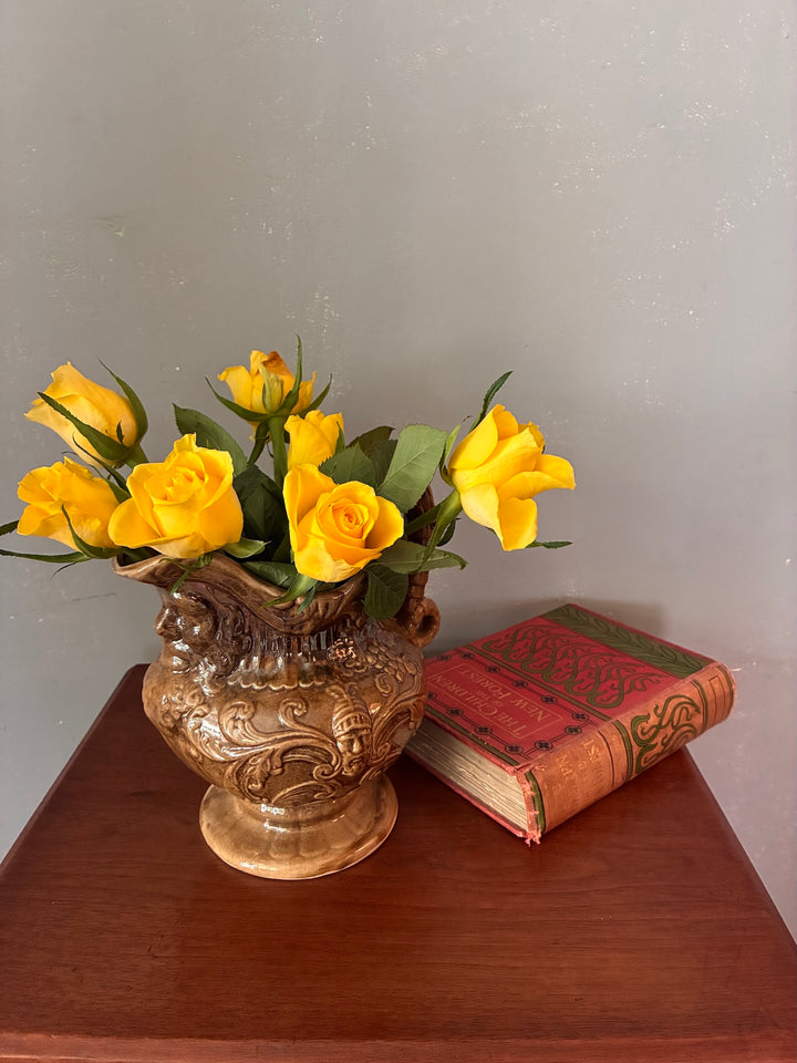 Vintage Neptune Pottery Jug with yellow roses on a wooden table next to an antique book.