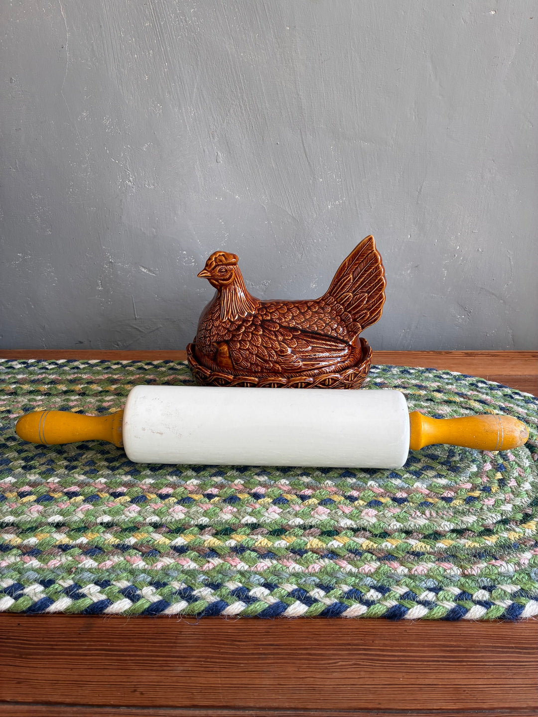 Vintage Nutbrown rolling pin with yellow handles on a handmade rug, accompanied by a decorative hen figurine.