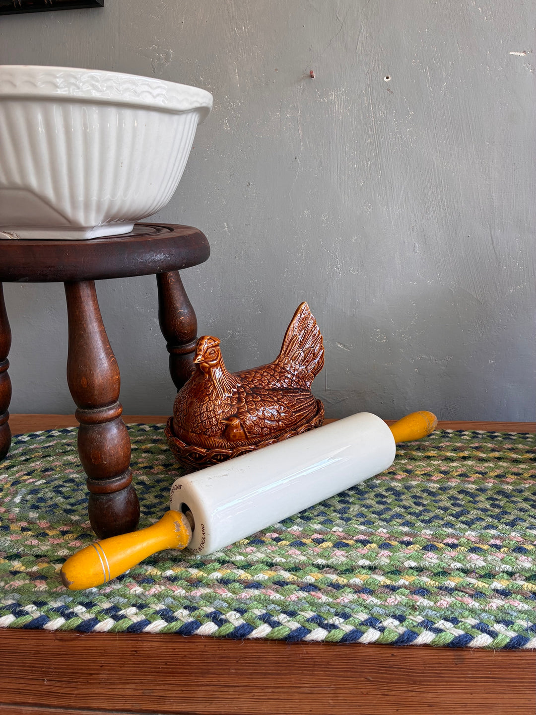 Vintage Nutbrown rolling pin with yellow handles on a colorful mat, with a brown ceramic hen and bowl in the background.