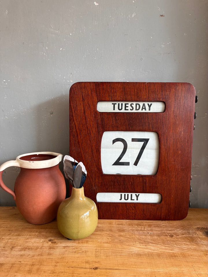 Vintage Wall Hanging Perpetual Calendar displayed with pottery on a rustic wooden table.