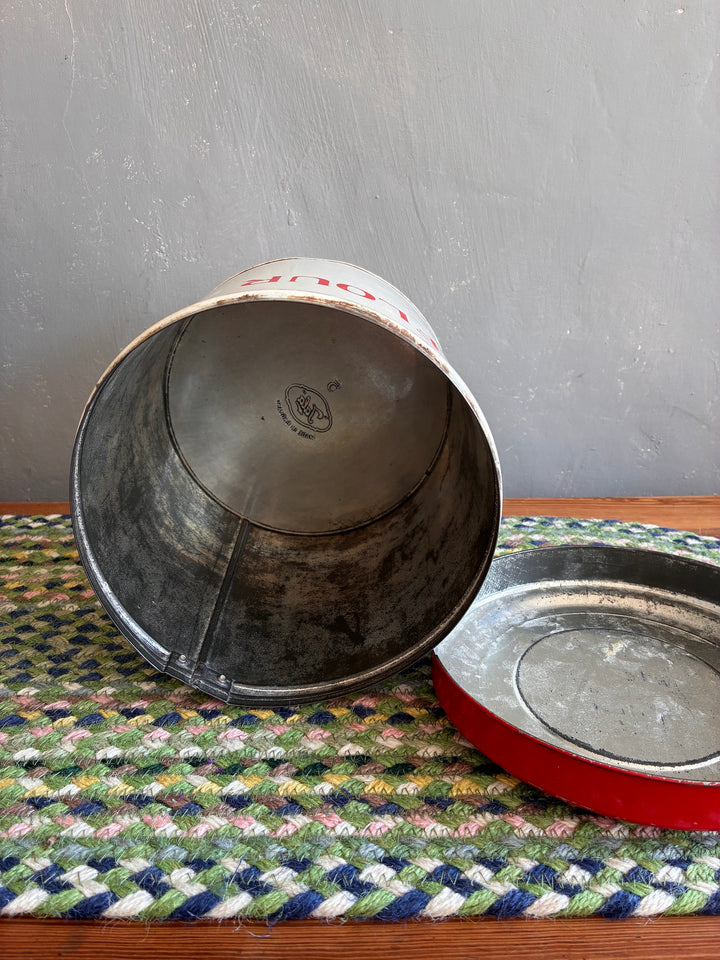 Interior view of a Vintage Red and White Tala Flour Bin on a woven mat, showcasing its worn finish and nostalgic design.