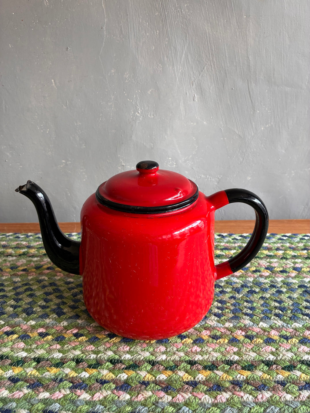 Vintage red enamel teapot with black handle and spout, perfect for serving tea and adding country charm.