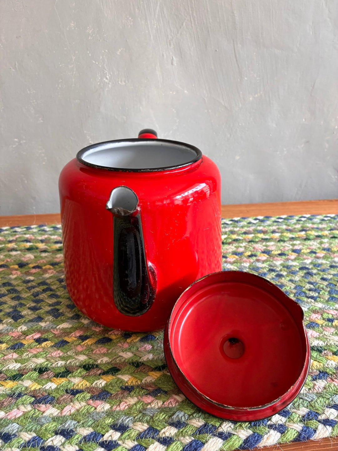 Vintage red enamel teapot with black handle and spout, perfect for serving tea or as a decorative vase.