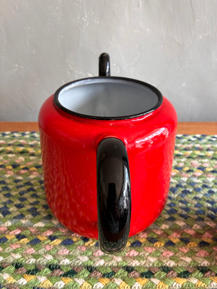 Vintage red enamel teapot with black handle and spout, perfect for serving tea or as a decorative vase.