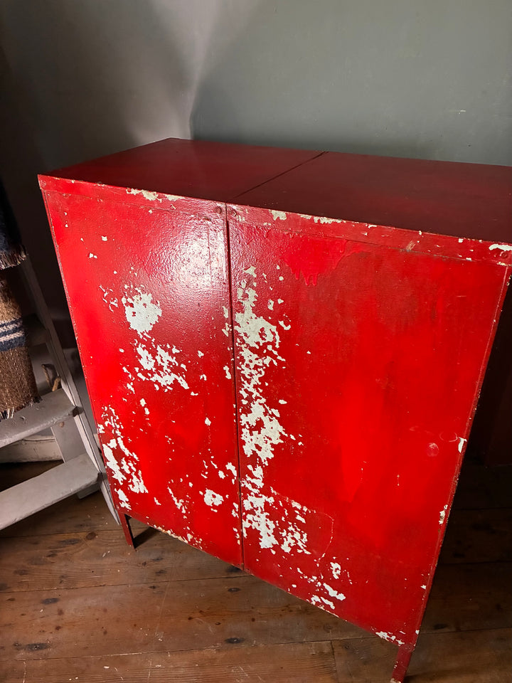 Red Metal Four Door Storage Locker displaying a distressed finish on a rustic wooden floor.