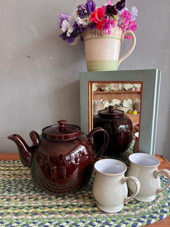 Vintage Brown Betty teapot with two mugs and flowers in a decorative setting, perfect for tea enthusiasts.