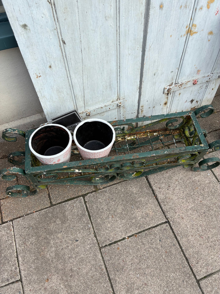 Vintage painted wrought iron trough planter with two floral pots on a stone patio, sourced from Source for the Goose Devon.