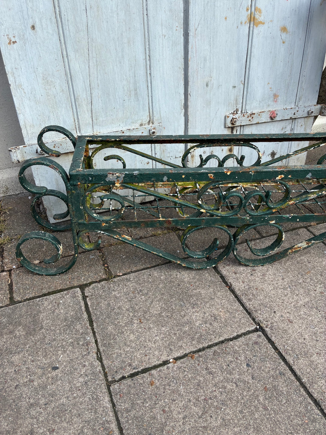 Vintage painted wrought iron trough planter showing intricate design and chippy green paint, ideal for rustic gardens.