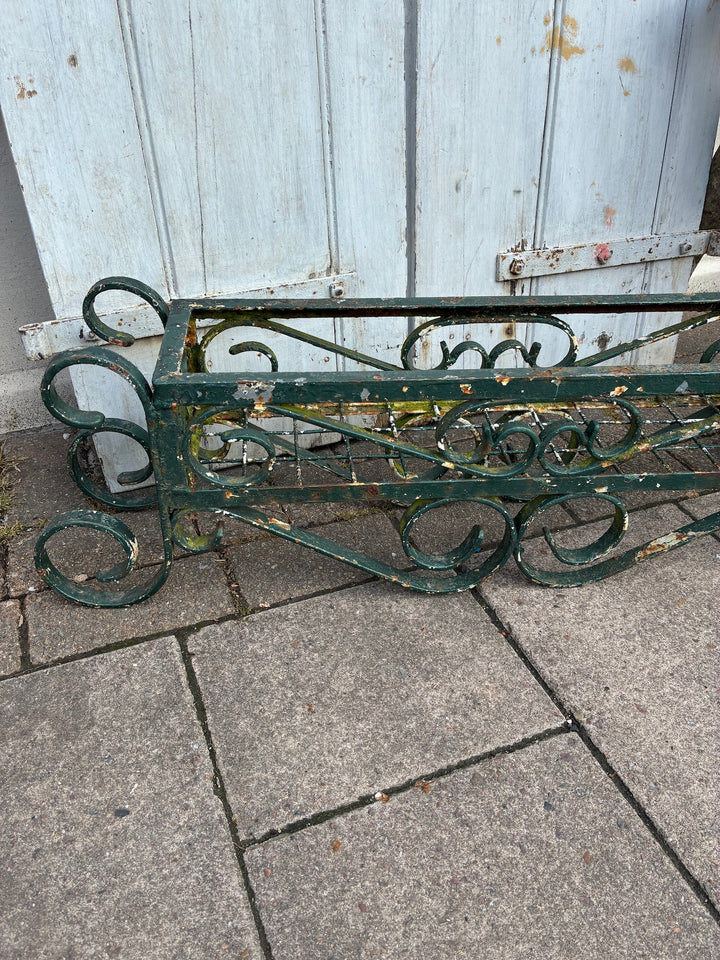 Vintage painted wrought iron trough planter showing intricate design and chippy green paint, ideal for rustic gardens.